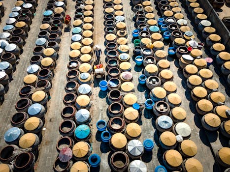 High angle view of workers maneuvering through rows of large covered barrels, creating an industrial pattern.