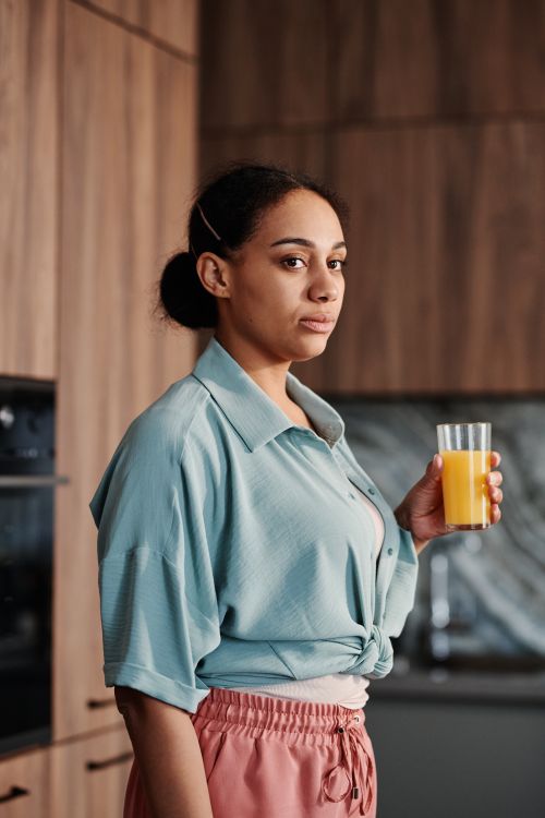Free Portrait of a stylish woman holding a glass of orange juice in a contemporary kitchen setting. Stock Photo