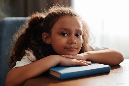 Free Adorable child with curly hair resting on a book, smiling gently. Stock Photo