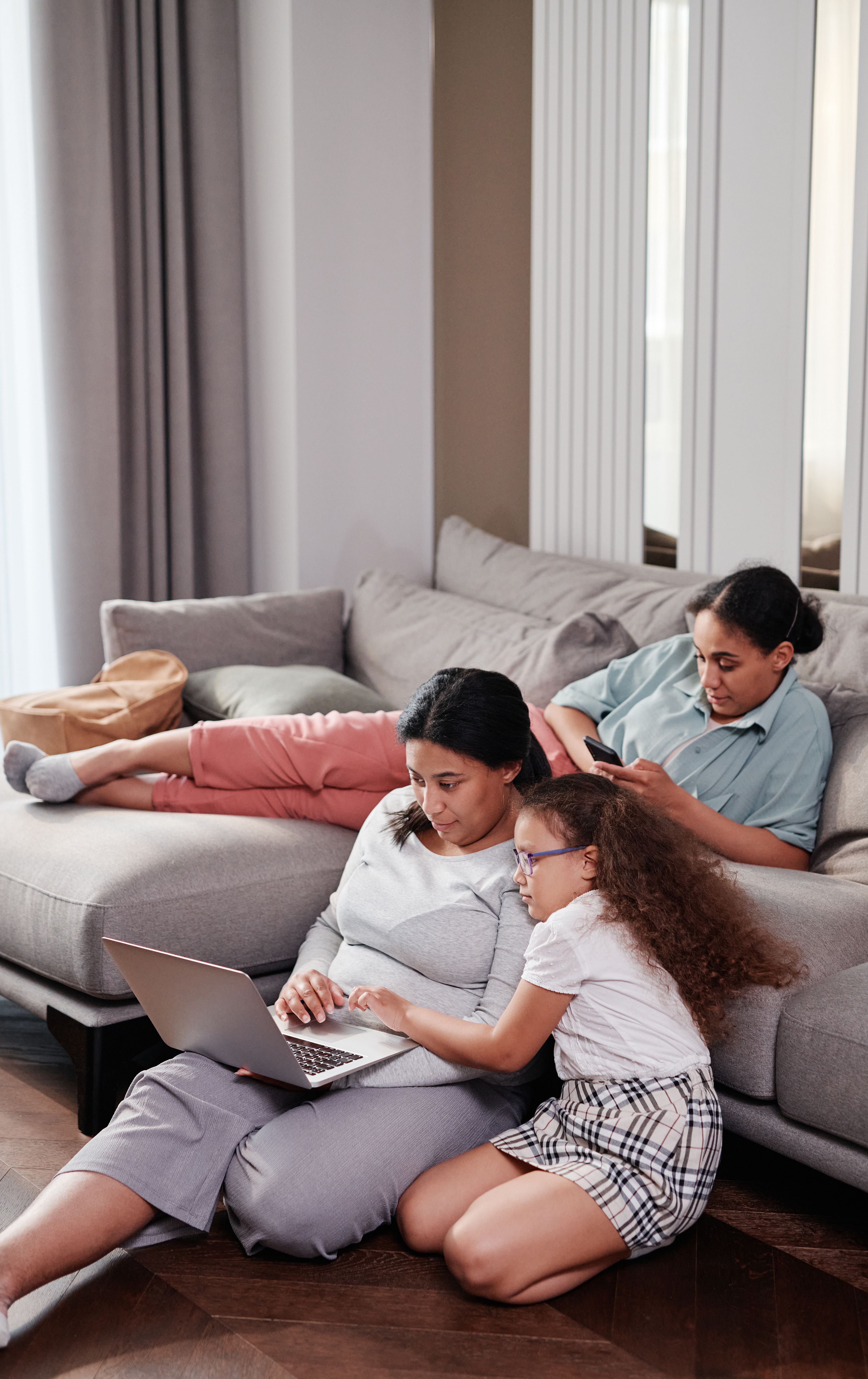 Family members sitting on a couch using a laptop and phone, enjoying quality time together indoors.