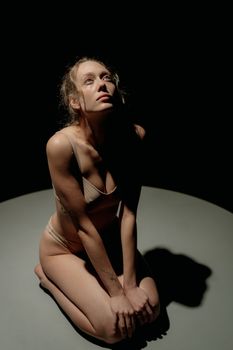 A moody artistic portrait featuring a woman in lingerie sitting in shadowed lighting.