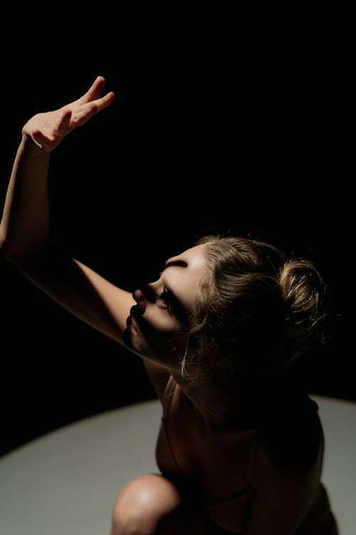 Free Artistic portrait of a woman with dramatic lighting and shadows, hand raised against a dark backdrop. Stock Photo
