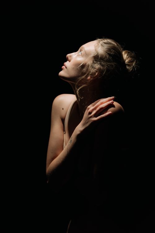 Free Artistic portrait of a woman looking upwards against a dark background, highlighting subtle elegance. Stock Photo