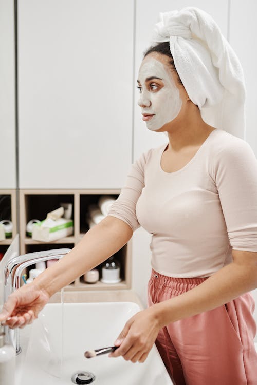 Woman with Face Mask Standing by Sink in Bathroom