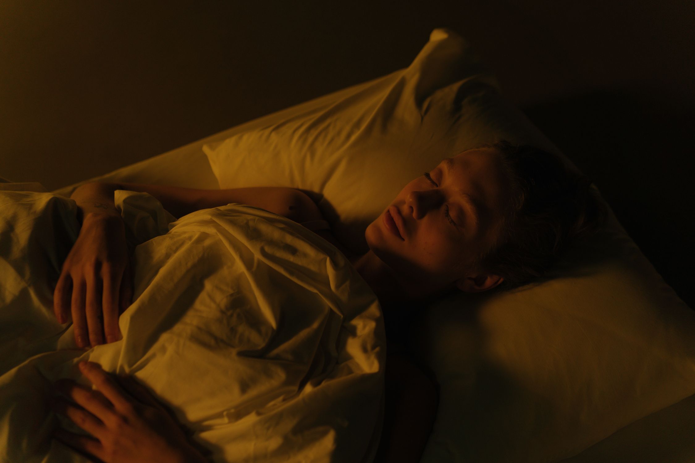 Mulher dormindo tranquilamente em quarto com iluminação suave, destacando a importância do sono profundo para a limpeza metabólica cerebral.
