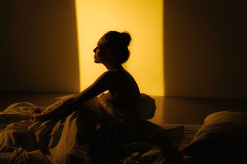 Free A silhouette of a woman sitting in bed with warm sunlight streaming in. Stock Photo
