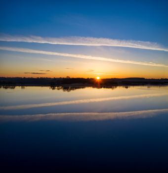 A breathtaking sunset reflects on a calm lake, creating a serene and peaceful scene.