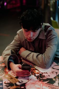 A man in a coat gazes at his smartphone while seated at a colorful cafe table.