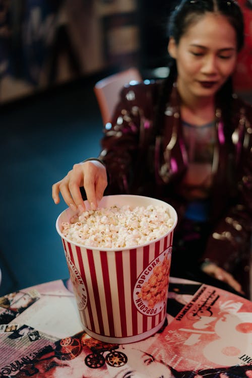 A Woman Sitting at the Table Getting a Popcorn from a Bucket