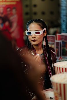 Stylish woman wearing 3D glasses enjoying popcorn at a bustling cinema.