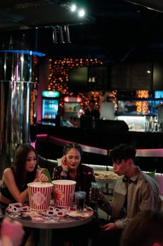 Three friends enjoying popcorn and drinks in a stylish bar during a night out, capturing a lively atmosphere.