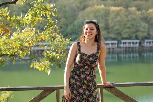 Free Young woman in a floral dress smiling near a serene lakeside view. Stock Photo