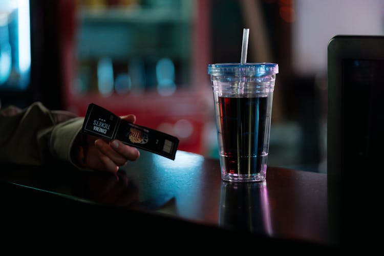 A Person At A Counter With A Cup Of Beverage Holding Cinema Ticket