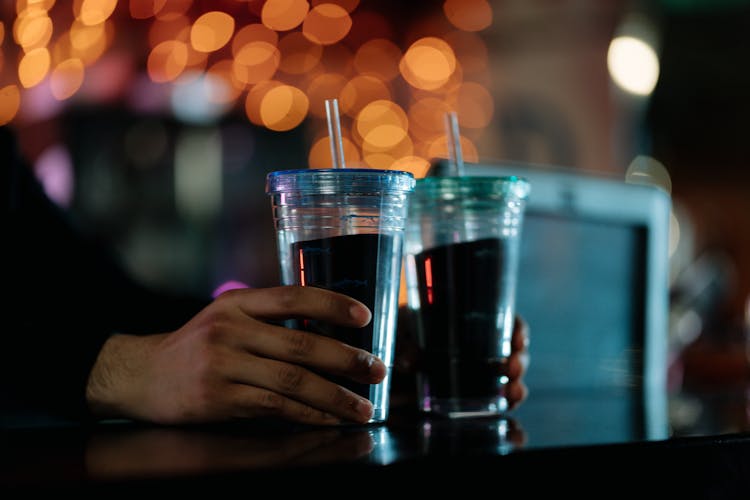 A Person Holding Clear Disposable Cups With Beverages