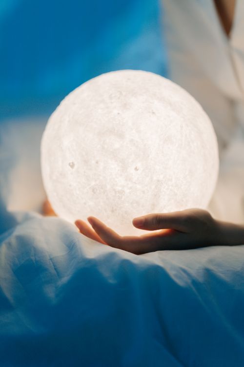Free A person holding a glowing spherical lamp against a serene blue background, creating a dreamy atmosphere. Stock Photo