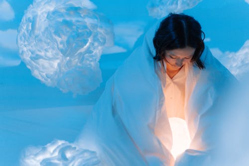 A Woman Covered with White Blanket Looking at the Moon Lamp she is Holding