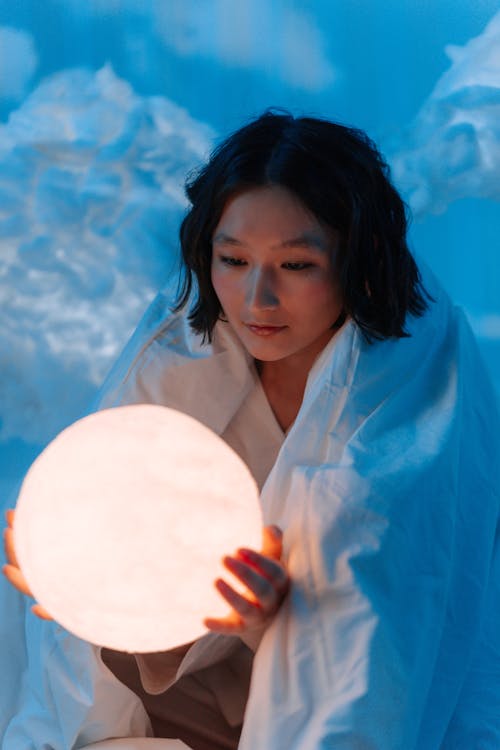 Woman in White Blanket Holding White Moon Lamp