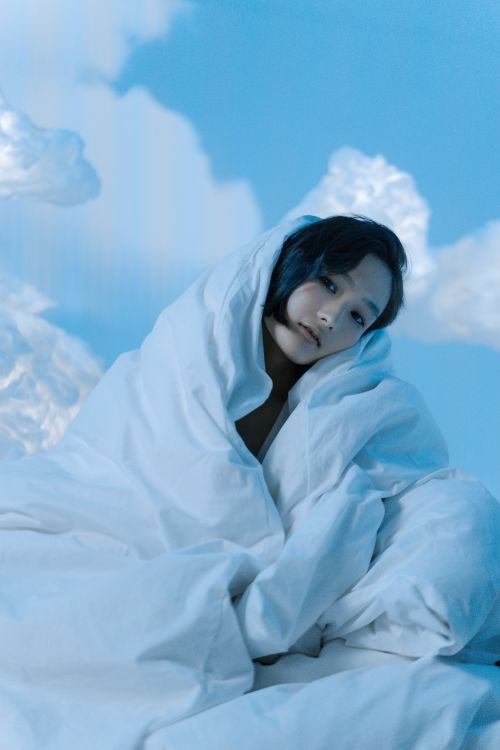 Free A serene portrait of a woman wrapped in a white blanket against a cloud-filled sky, evoking a peaceful dream. Stock Photo