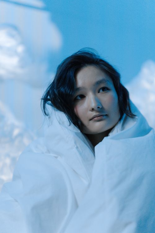 Free Portrait of an Asian woman wrapped in a blanket, bathed in serene blue lighting, evoking relaxation and introspection. Stock Photo