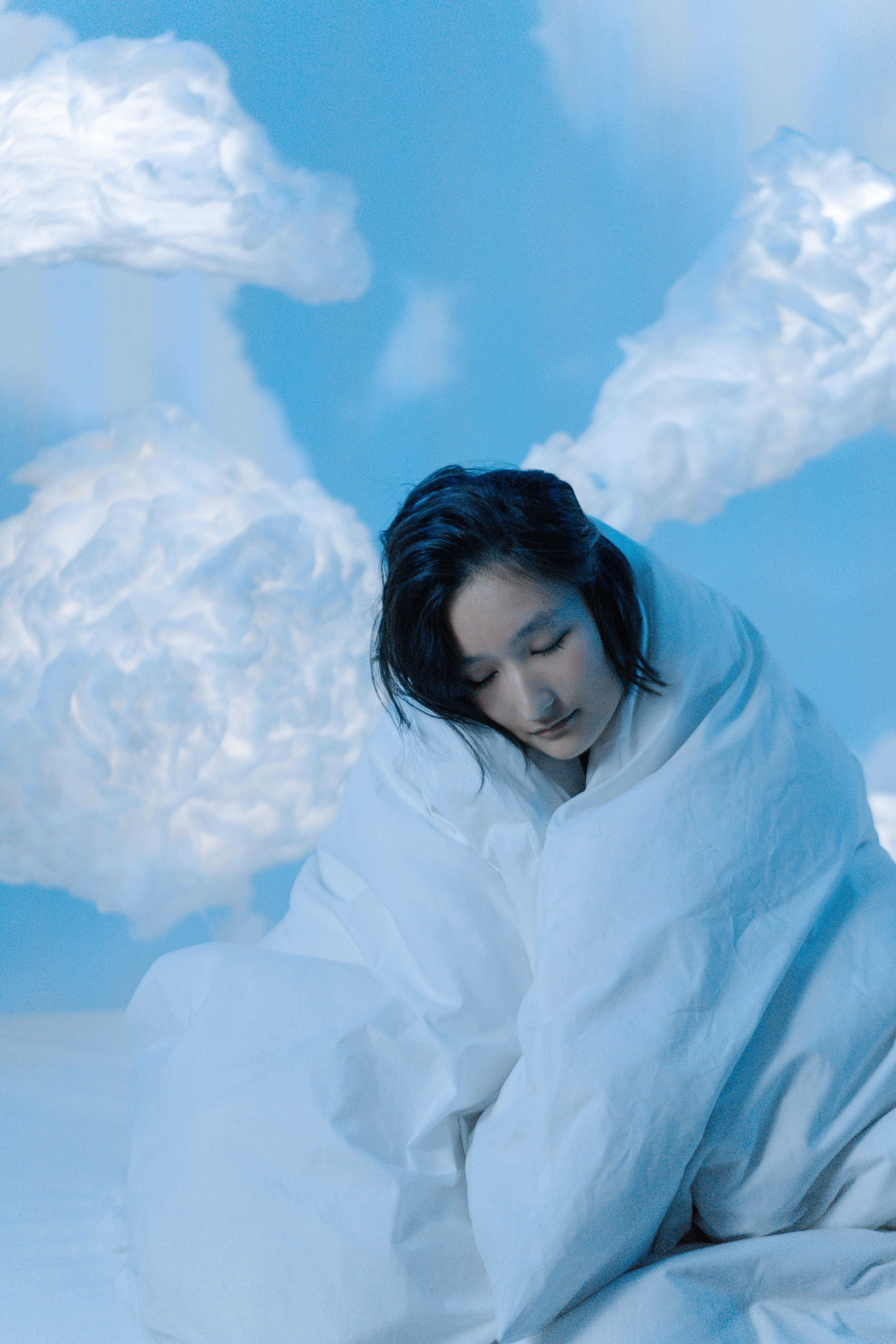 A serene woman wrapped in a white blanket amidst a fluffy cloud backdrop.