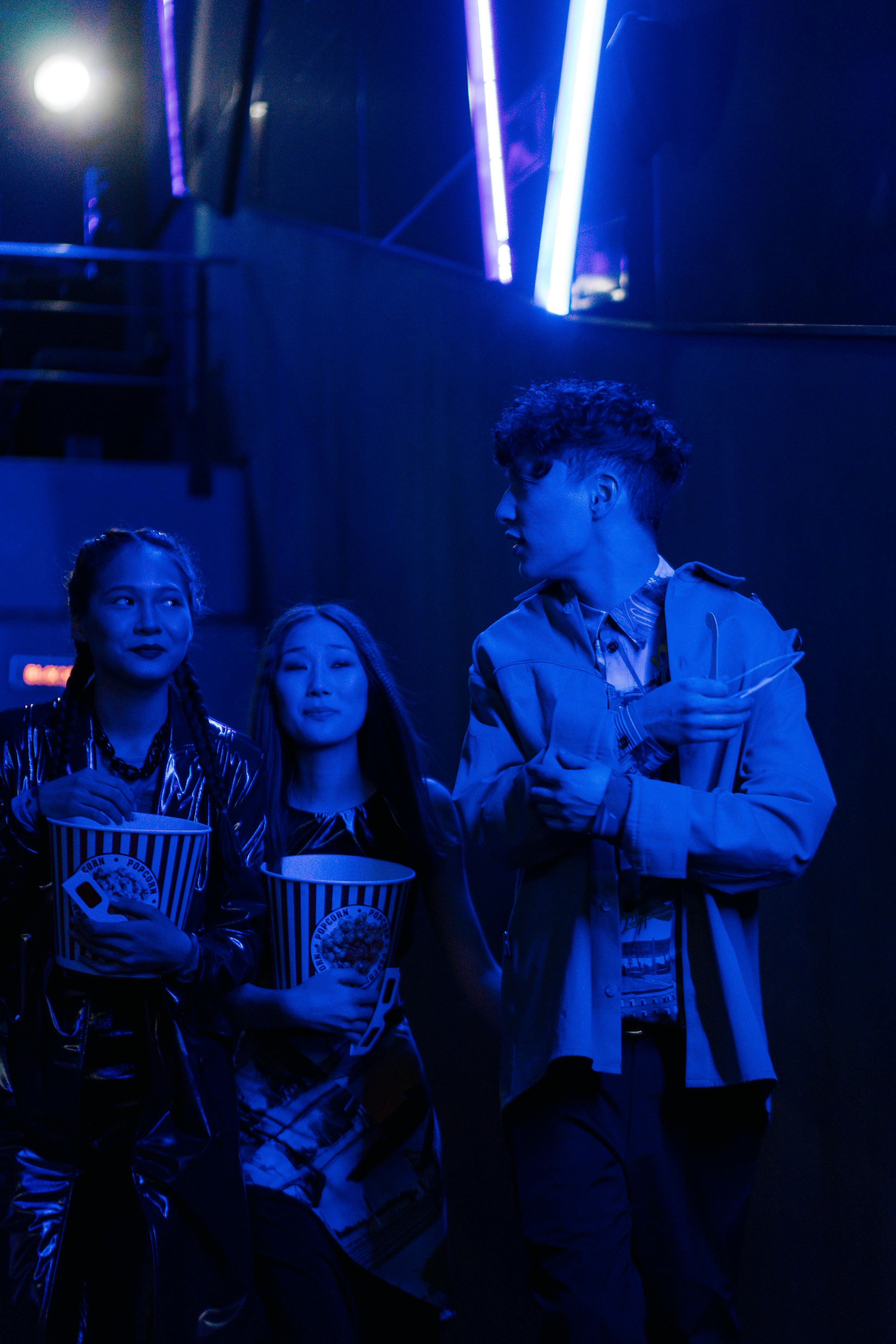 Free Group of friends enjoying popcorn in a cinema with vibrant blue lighting. Stock Photo