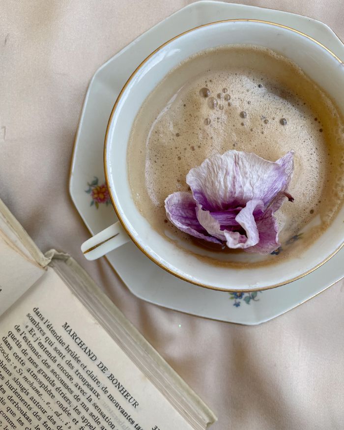 A cappuccino with a flower petal on top, beside an open book