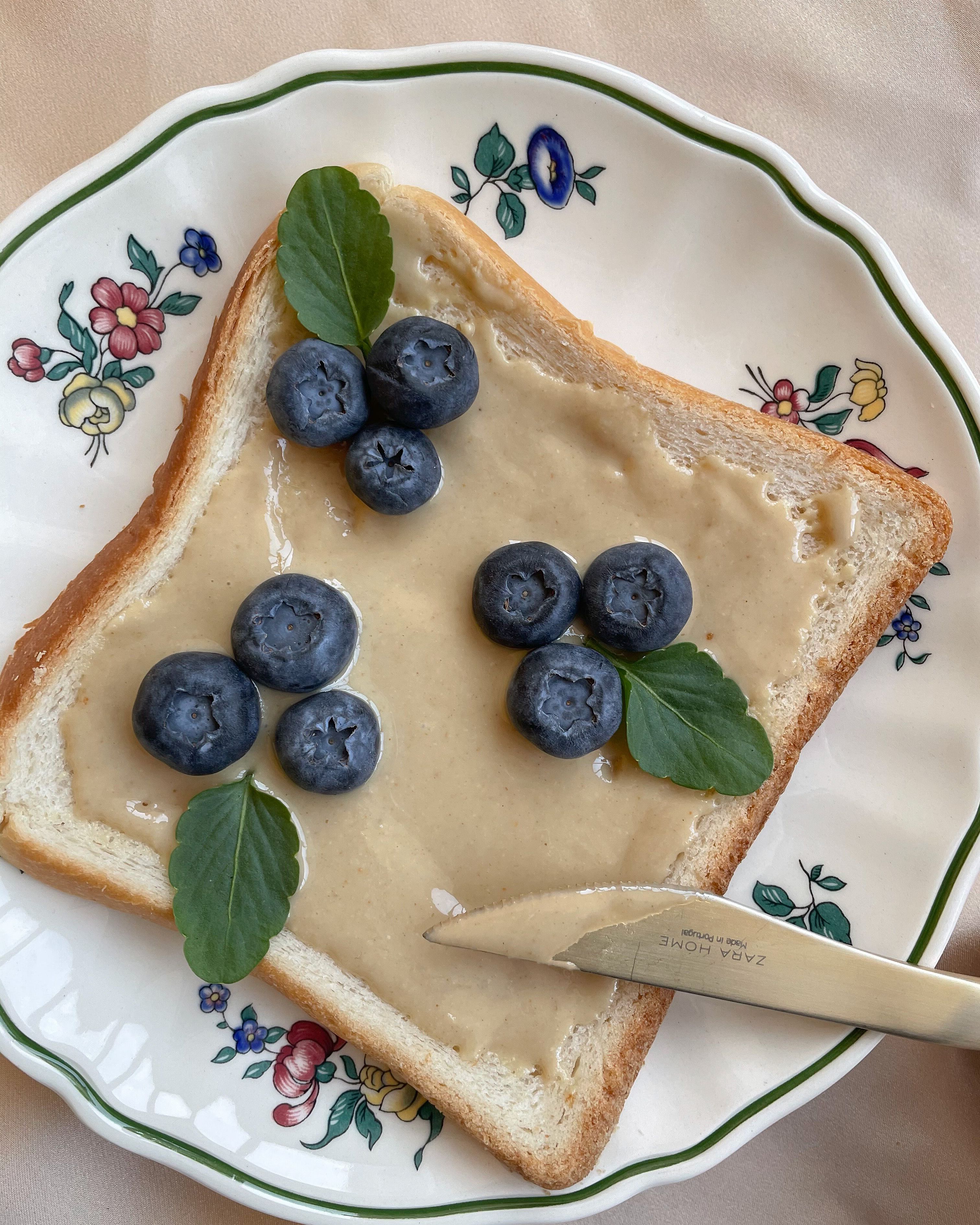 Close-up of peanut butter toast topped with blueberries and mint, on a decorative plate.