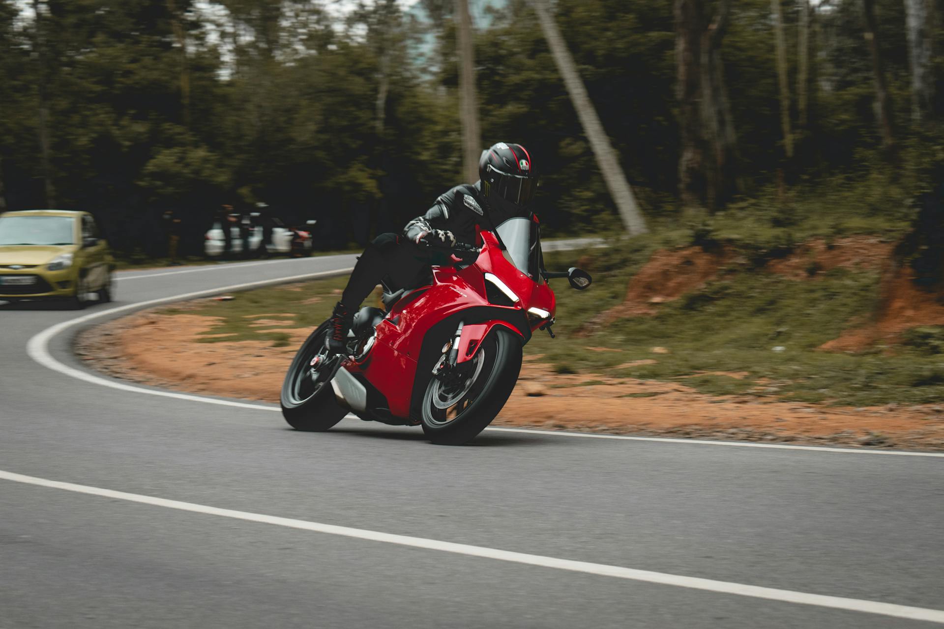 A motorcyclist in full gear leans into a turn on a scenic outdoor road.