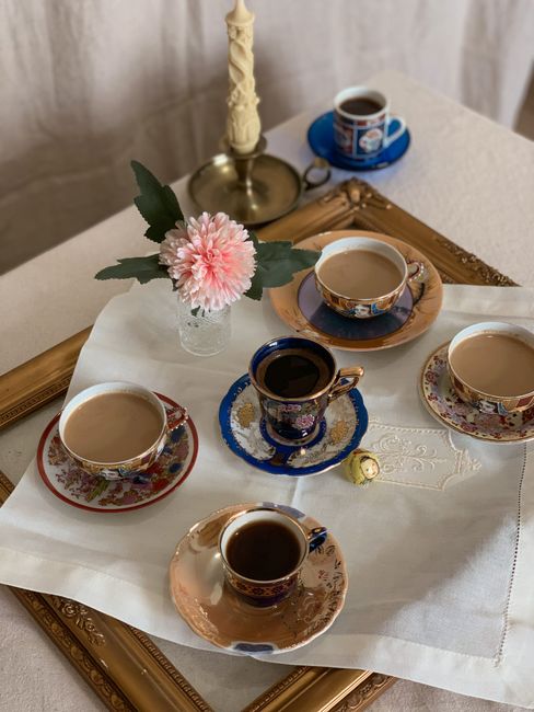 High angle of ceramic cups of coffee and flower in glass vase on tray placed on table near candle