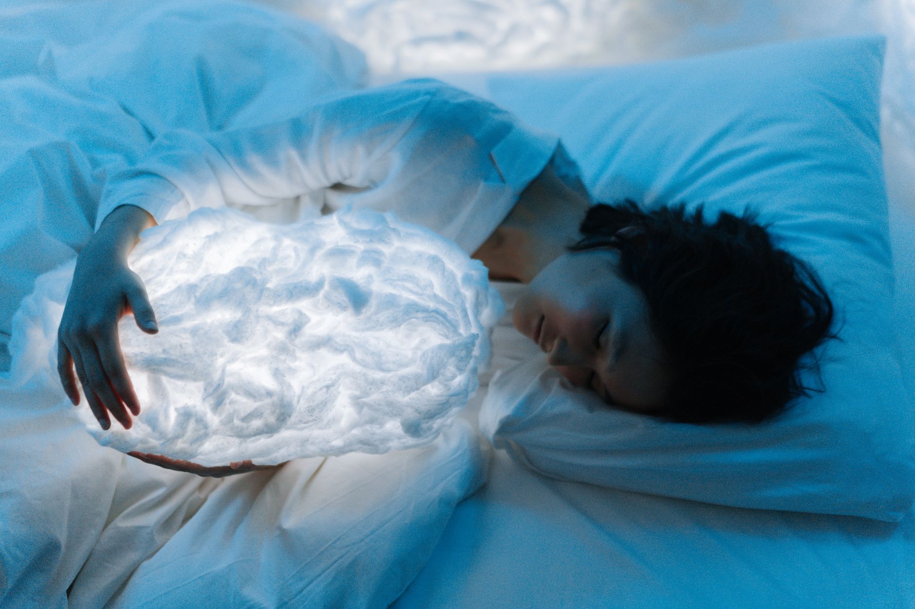 A woman peacefully sleeps holding a glowing cloud lamp, creating a serene nighttime atmosphere.