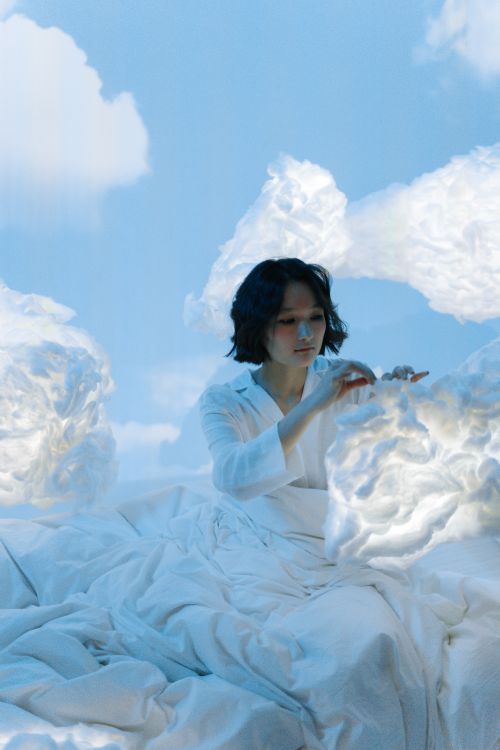 Free A woman in a white setting with cloud-like formations, evoking a dreamy atmosphere. Stock Photo