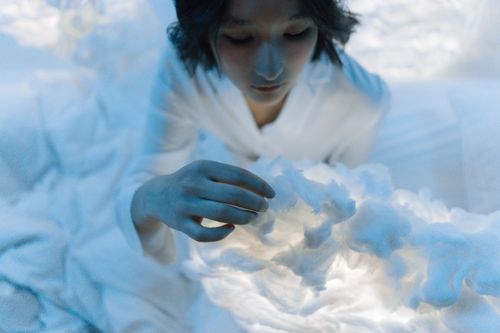 Free A woman in a soft blue light touching illuminated clouds creating a dreamy atmosphere. Stock Photo