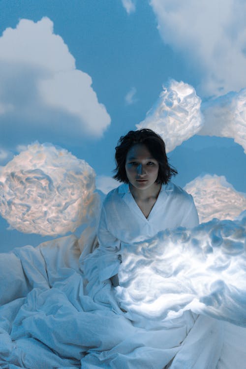 Woman Sitting on Bed with White Clouds and Blue Sky Wallpaper on Background