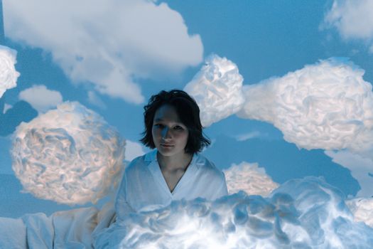 A woman sits surrounded by fluffy clouds, creating a dreamlike and imaginative scene.