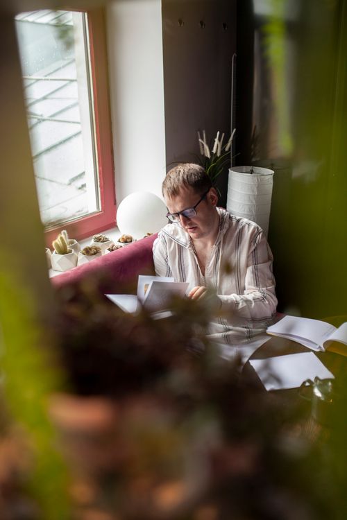 Free A man reading a book in a comfortable, well-lit home setting with plants. Stock Photo