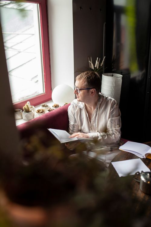 Free Man in casual attire reading by a window, offering a serene and reflective ambiance. Stock Photo