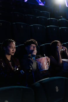 Three young adults enjoying popcorn while watching a movie in a theater.