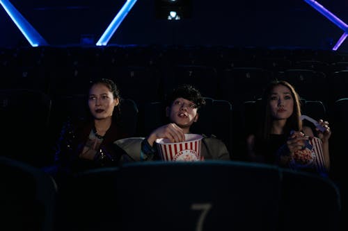 Free Three Friends Watching at a Movie Theater While Eating Popcorn Stock Photo