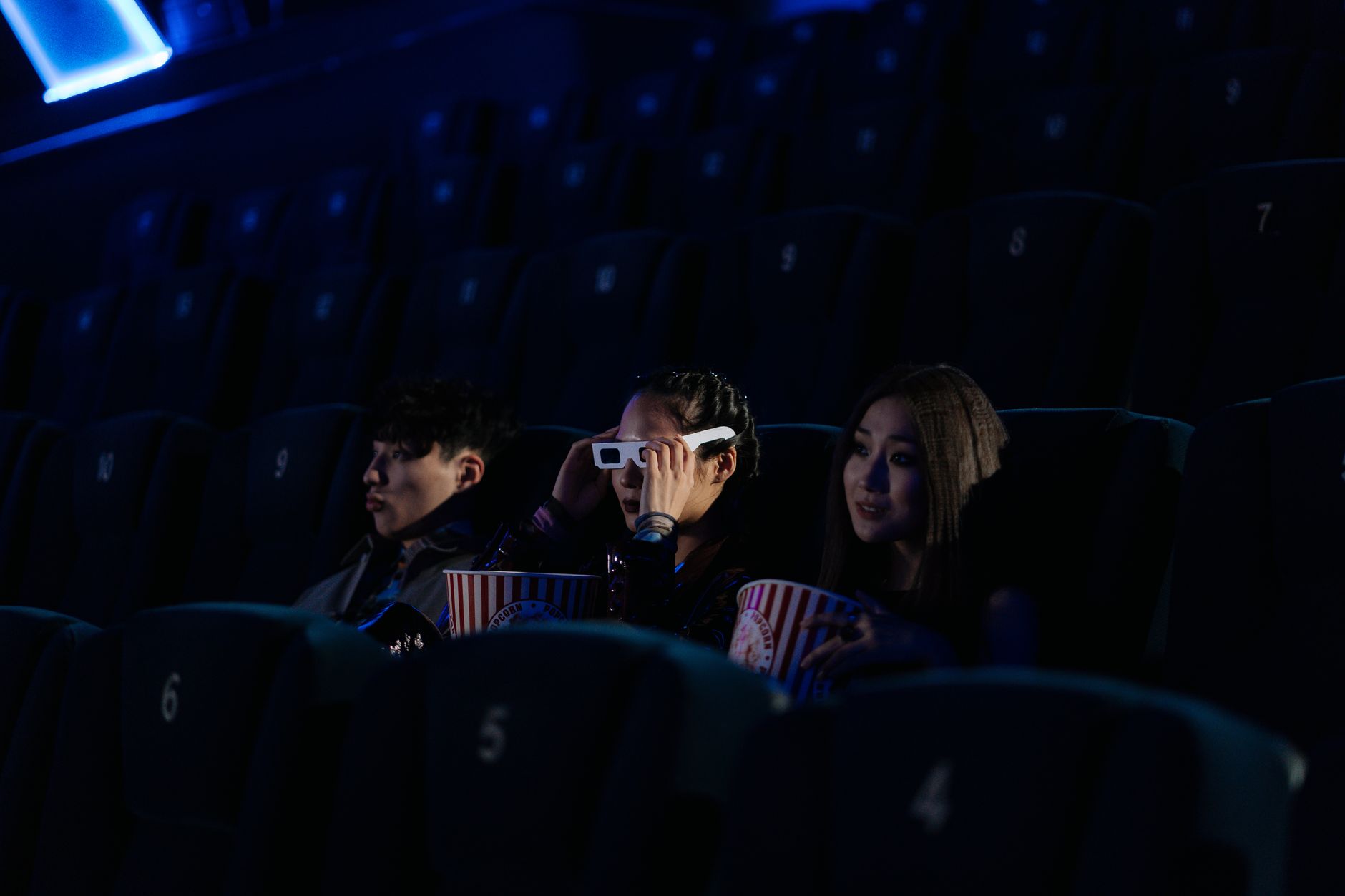Group of friends watching a 3D movie and enjoying popcorn in a dimly lit theater.