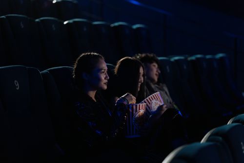 Free Group of friends watching a movie in a dark cinema, enjoying popcorn. Stock Photo