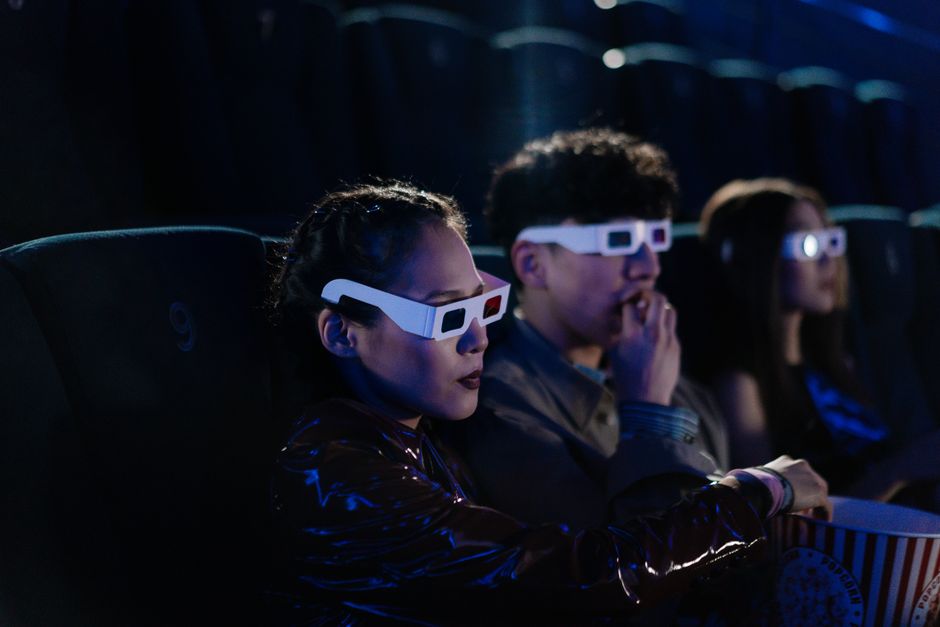 Grupo de pessoas assistindo a um filme ou evento em uma sala de cinema com óculos 3D, destacando o entretenimento e experiências visuais imersivas.