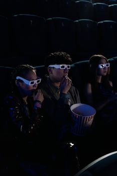 Group of friends enjoying a 3D movie with snacks in a dark theater.