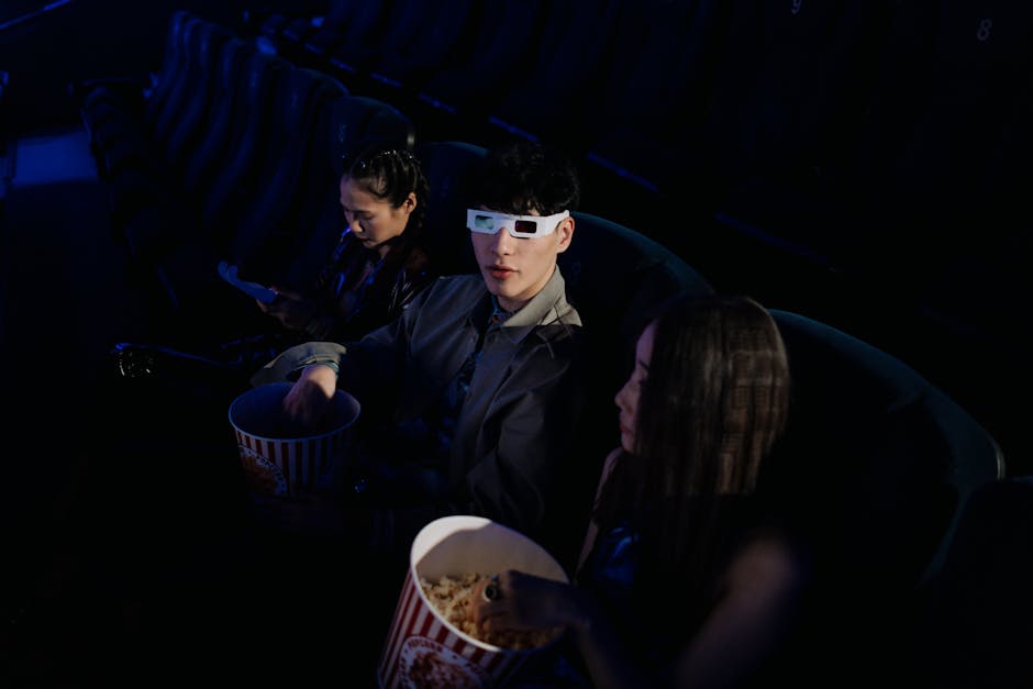 A group of young adults watching a 3D movie at a cinema, enjoying popcorn.