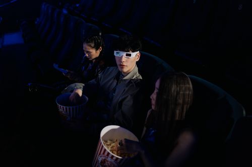 Free A group of young adults watching a 3D movie at a cinema, enjoying popcorn. Stock Photo