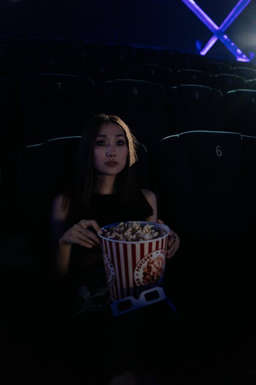 A Woman Sitting on a Cinema while Holding a Bucket of Popcorn