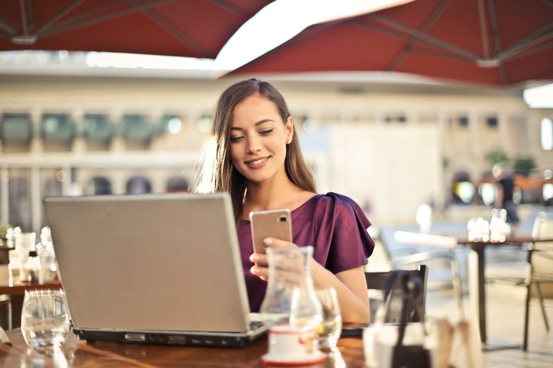 Woman enjoying remote work at a café, using a laptop and smartphone.