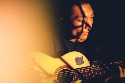 Selective Focus Photo of a Man Playing an Acoustic Guitar