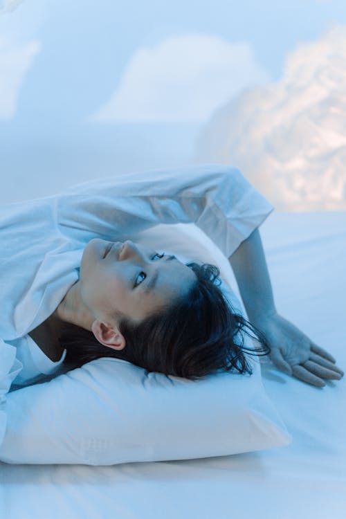A Woman in White Long Sleeves Lying on a White Textile