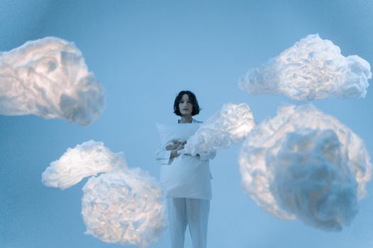 A serene portrait of an Asian woman surrounded by illuminated clouds in a conceptual, dreamy setting.