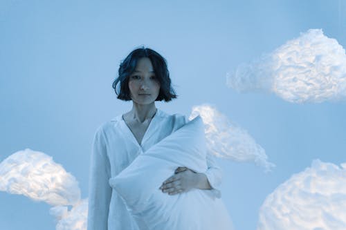 Woman in White Pajamas Holding a Pillow Near The Clouds